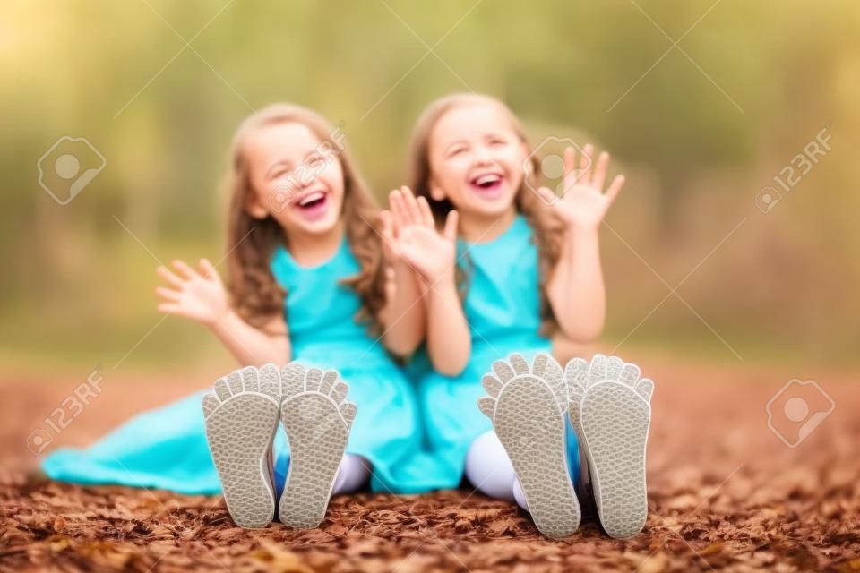 Twee kleine meisjes die op de grond zitten en hun hielen laten zien lachen