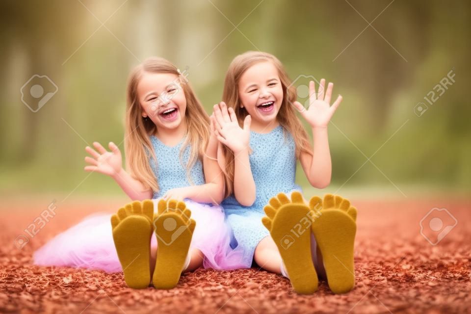 Twee kleine meisjes die op de grond zitten en hun hielen laten zien lachen