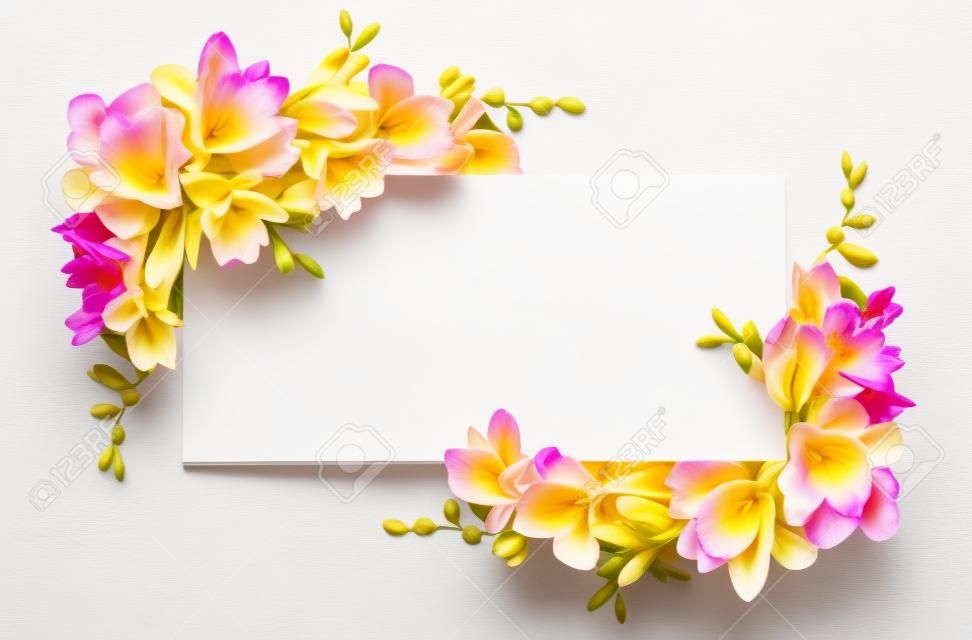 白い背景で隔離の白いカードのコーナーアレンジメントでピンクと黄色のフリージアの花
