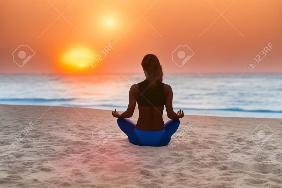 Young women do yoga on the beach at sunrise. Healthy lifestyle concept