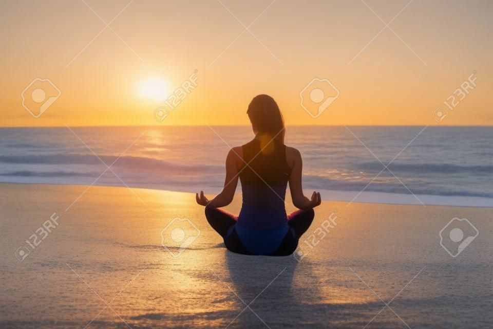 Les jeunes femmes font du yoga sur la plage au lever du soleil. Concept de mode de vie sain