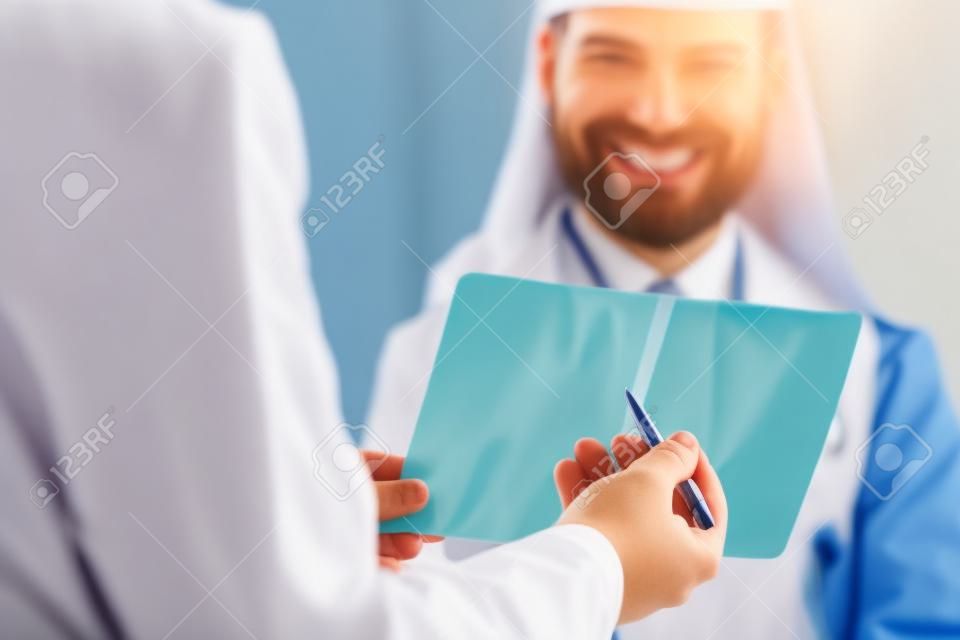 Close-up of doctor hands holding skiagram. Surgeon talking about wrist trauma. Smiling intern listening carefully to traumatologist. Traumatology and health care concept