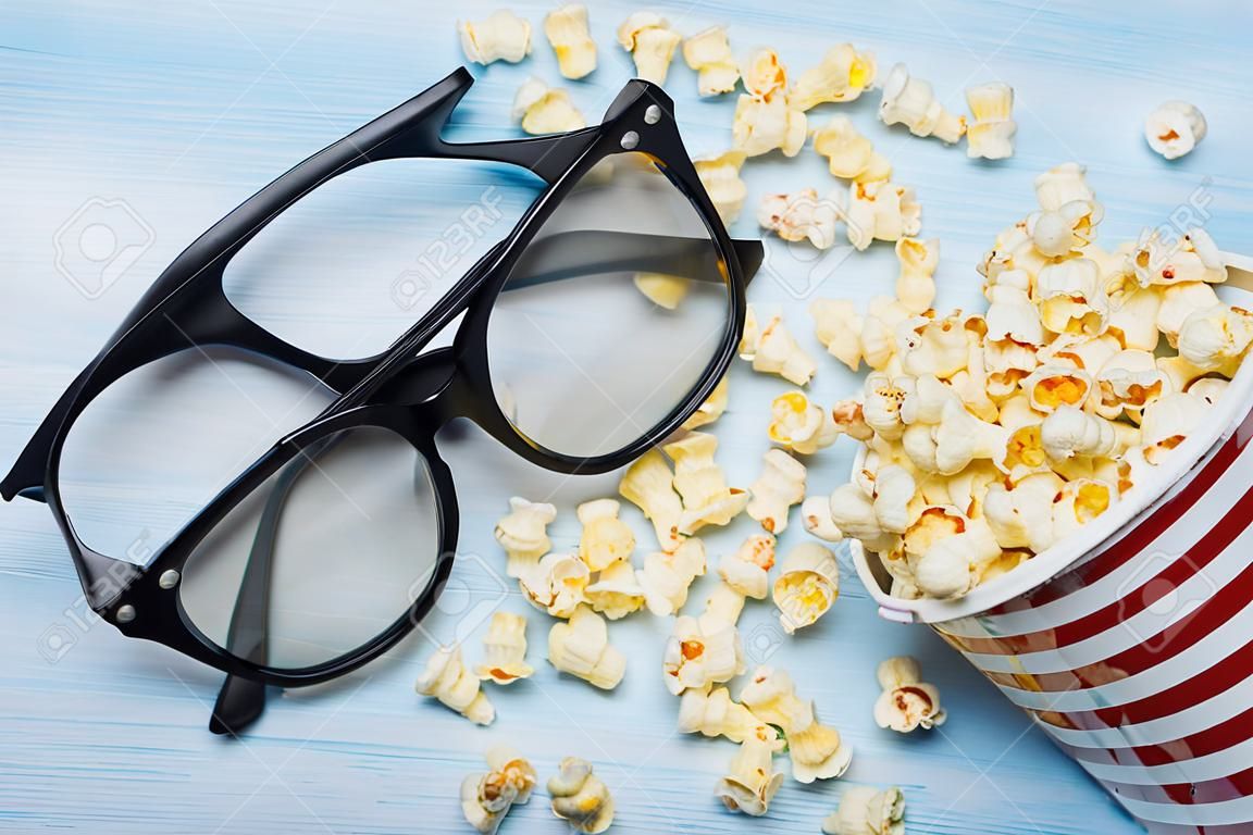 un secchio di popcorn sparsi su uno sfondo chiaro e un paio di occhiali 3d
