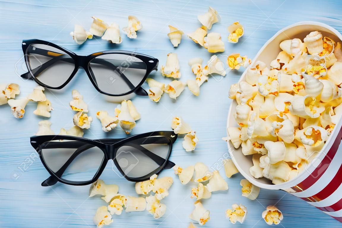 a bucket of scattered popcorn on a light background and a pair of 3d glasses