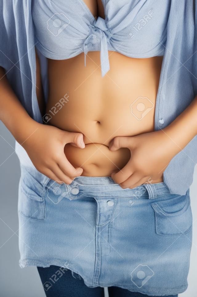 A young woman is holding the fat rolls on her stomach. 