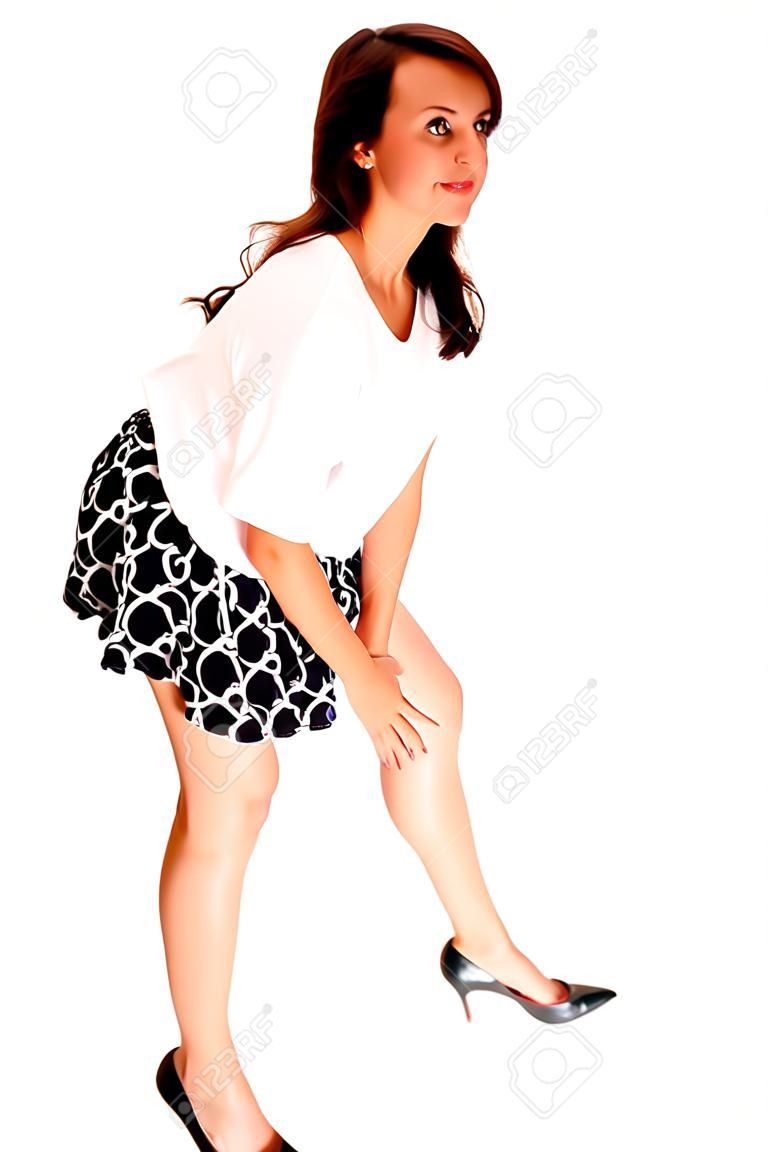 Uma menina adolescente bonita em uma blusa branca e saia curta que está isoladapara o fundo branco, curvando-se para baixo.