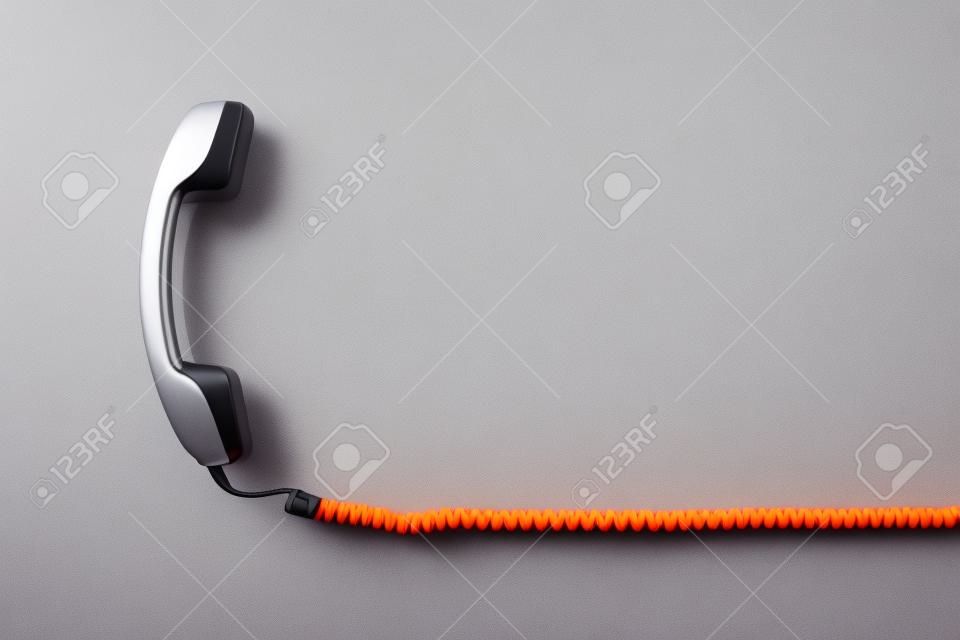 Szara słuchawka z przewodem na pomarańczowym tle. leżał płasko. retro sprzęt komunikacyjny.