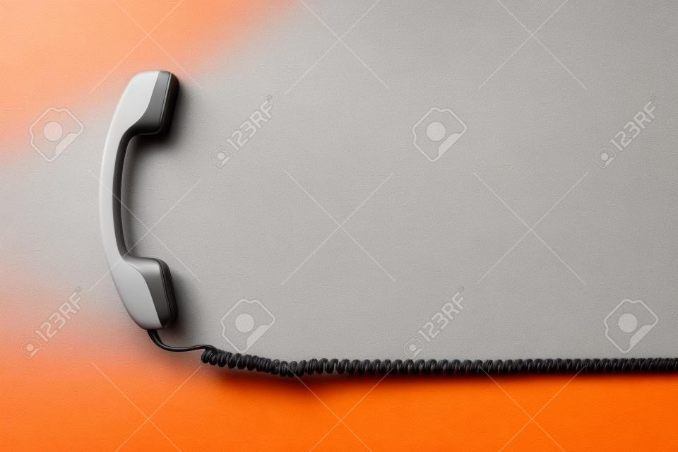 Szara słuchawka z przewodem na pomarańczowym tle. leżał płasko. retro sprzęt komunikacyjny.