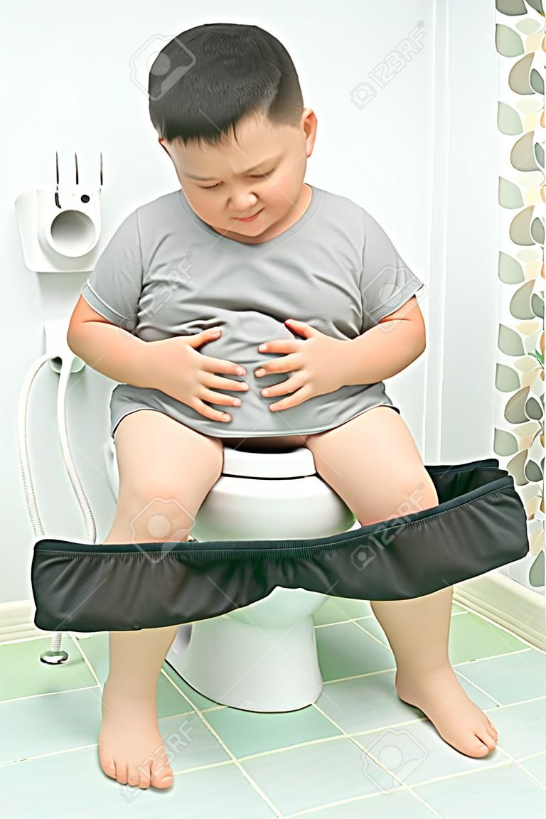 El niño gordo sufre de estómago y se sienta en el inodoro, diarrea, estreñimiento y concepto de salud.