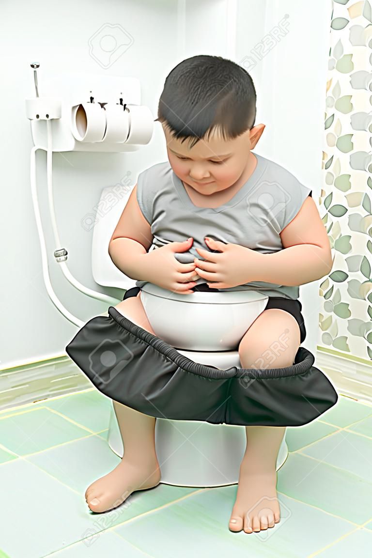 太った男の子は胃に苦しみ、トイレ、下痢便秘と健康概念に座ります。