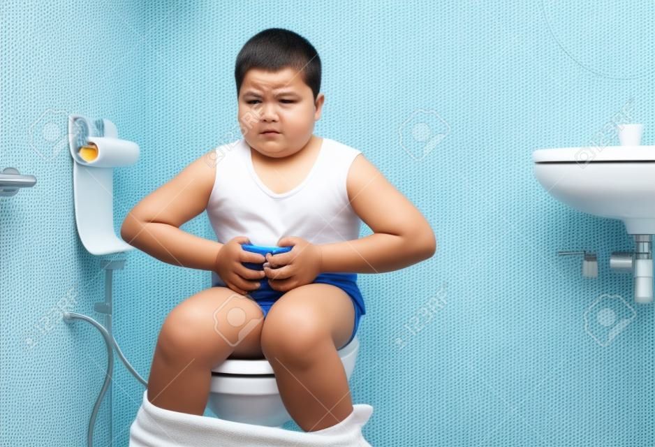 gruby chłopiec cierpi na żołądek i siedzi w toalecie, biegunkę, zaparcia i koncepcję zdrowia..