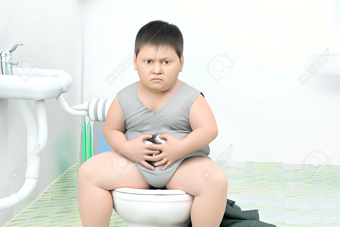 gruby chłopiec cierpi na żołądek i siedzi w toalecie, biegunkę, zaparcia i koncepcję zdrowia..
