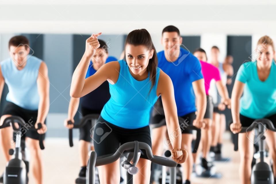 五人组——男女运动员——在健身房或健身俱乐部运动，锻炼腿部，做心脏训练，教练在前面。