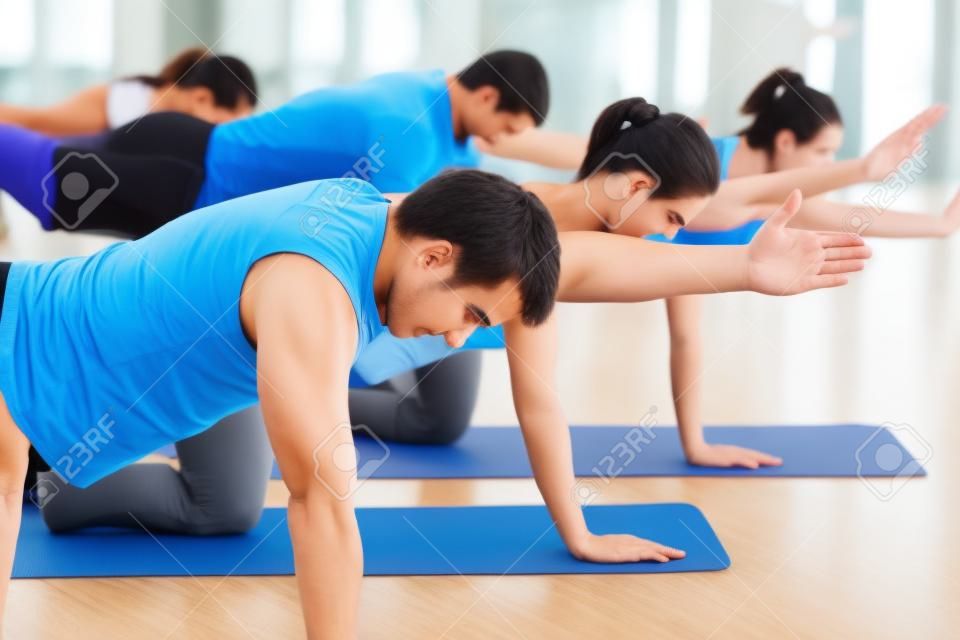 Group of five people is doing stretching exercises in fitness club on gym mats