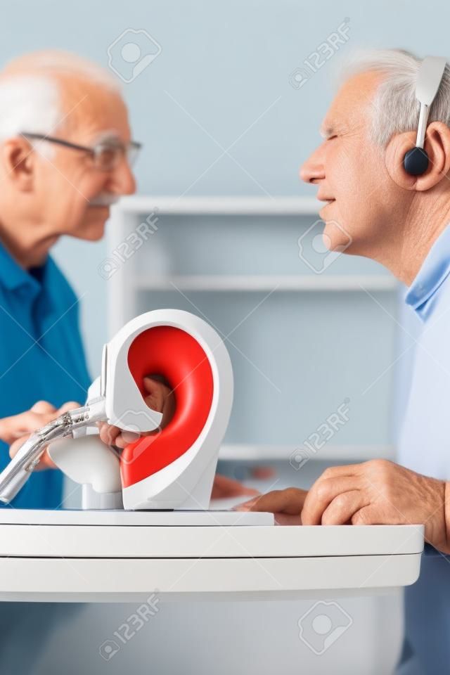 Ältere Menschen oder Rentner mit einem Hörproblem machen einen Hörtest und kann ein Hörgerät benötigen, im Vordergrund ist ein Modell eines menschlichen Ohres