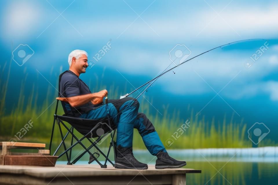 Homme de pêche au lac assis sur la jetée près de l'eau