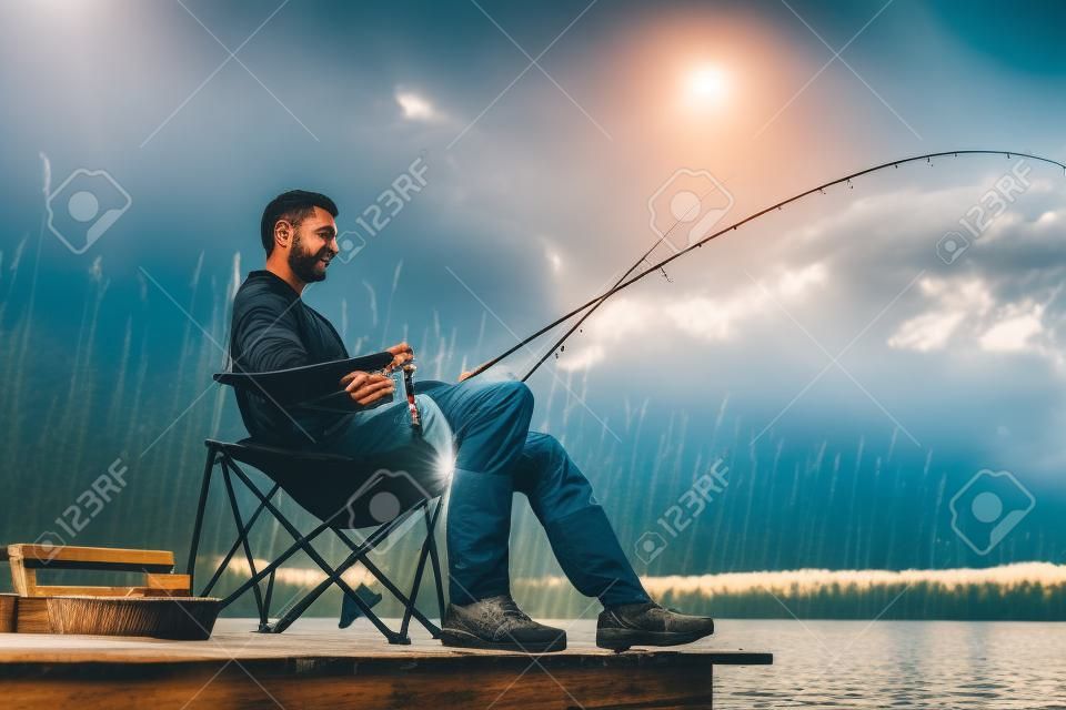 Homme de pêche au lac assis sur la jetée près de l'eau