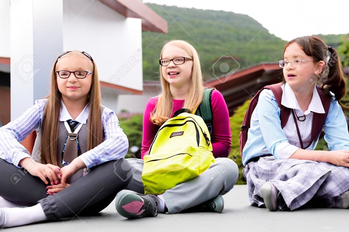 Schoolgirls sitting in schoolyard at school having recess and talking