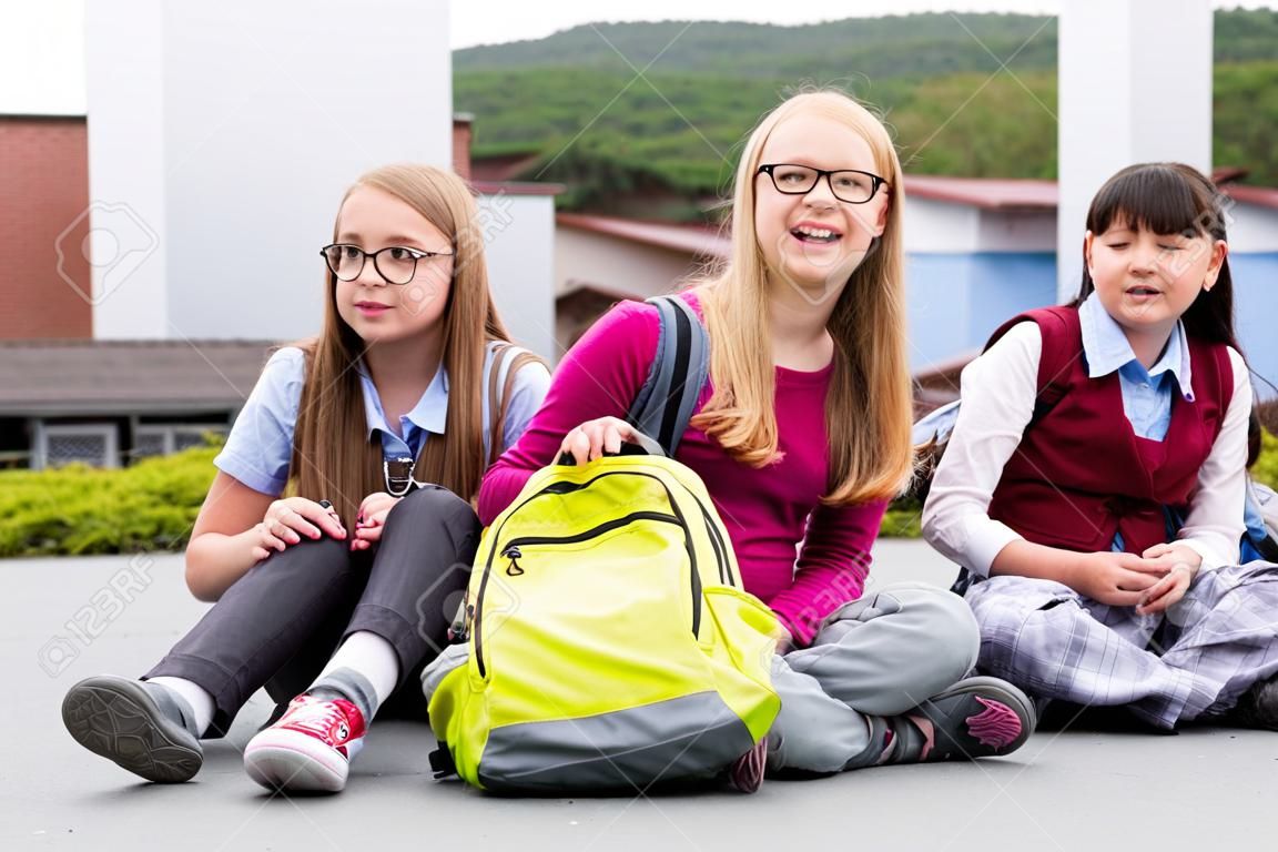 Schoolgirls sitting in schoolyard at school having recess and talking