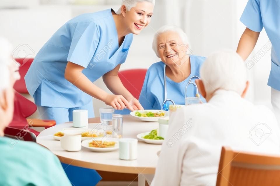 Groep senioren die voedsel hebben in het verpleeghuis, een verpleegster serveert