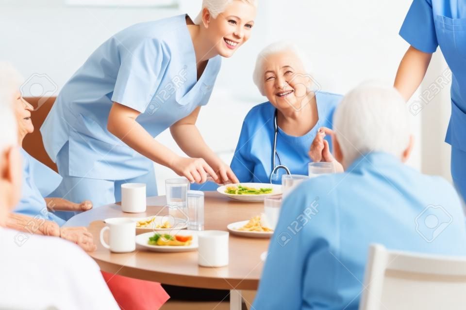 Gruppo di anziani che hanno il cibo in casa di cura, un infermiere sta scontando