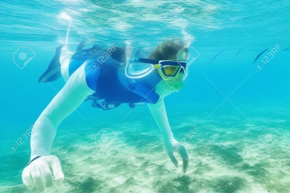 Mulher que snorkeling sobre o assoalho do mar tropical em suas férias de verão