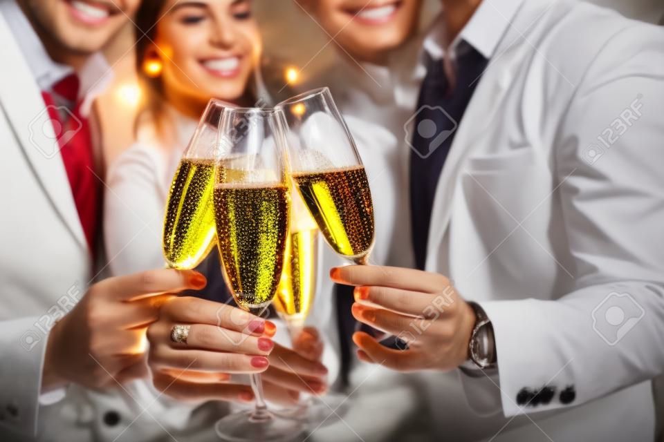 Männer und Frauen feiern Geburtstag oder Silvesterparty beim Klirren von Gläsern mit Sekt