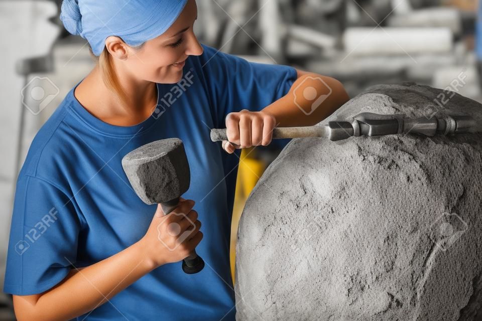 Female stonemason working on boulder with sledgehammer and iron