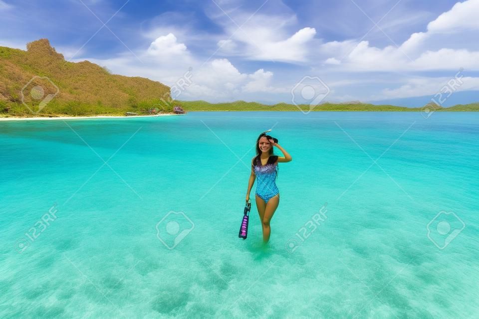 微笑美丽的年轻女子，同时在印度尼西亚科莫多岛的暑假期间在粉红色的海滩上举行浮潜设备微笑