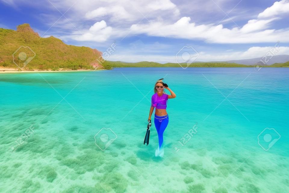 微笑美丽的年轻女子，同时在印度尼西亚科莫多岛的暑假期间在粉红色的海滩上举行浮潜设备微笑