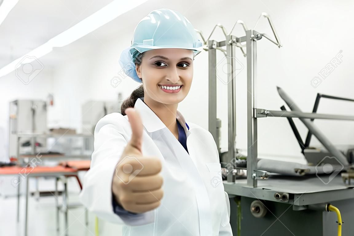Porträt einer glücklichen weiblichen Fertigungsspezialistin mit Daumen hoch als Zeichen für positives Feedback nach Qualitätskontrolle in einer modernen Fabrik