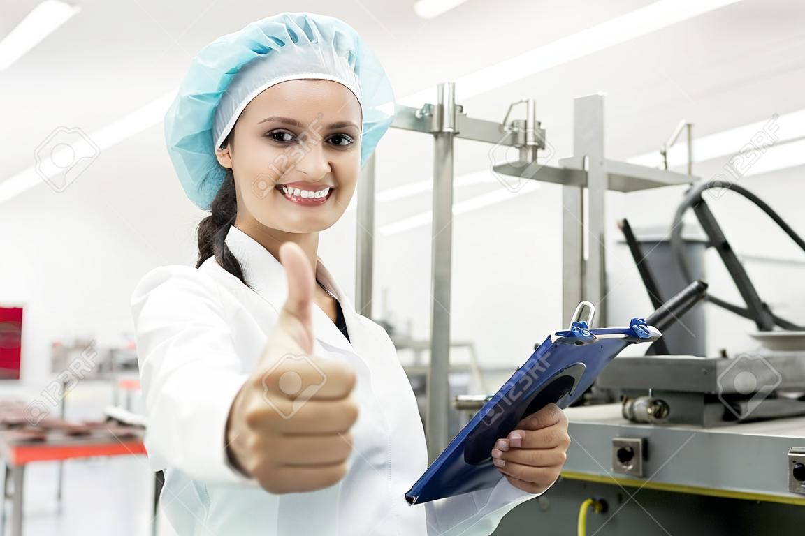 Porträt einer glücklichen weiblichen Fertigungsspezialistin mit Daumen hoch als Zeichen für positives Feedback nach Qualitätskontrolle in einer modernen Fabrik