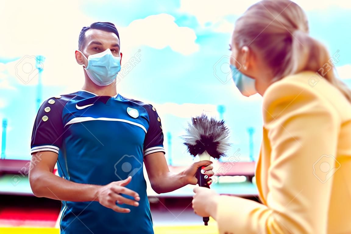 Reporter doing interview with football player during covid-19 wearing masks in soccer stadium