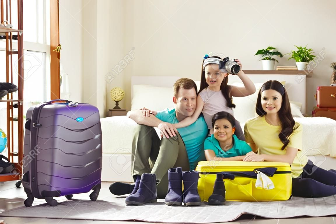 여행 가방 가방 휴가 여행 준비에 포장된 옷으로 둘러싸인 집 거실 바닥에 앉아 여름 휴가 여행을 준비하는 아이들과 함께 행복한 가족의 초상화