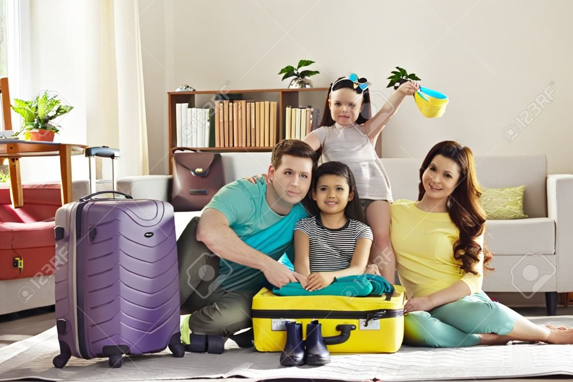 여행 가방 가방 휴가 여행 준비에 포장된 옷으로 둘러싸인 집 거실 바닥에 앉아 여름 휴가 여행을 준비하는 아이들과 함께 행복한 가족의 초상화