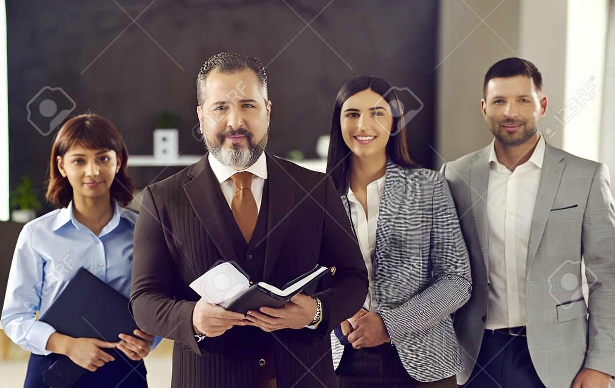 Portrait of a confident adult business leader with a team of employees standing behind him. Man and his business team looking at the camera and smiling. Concept success and team spirit.