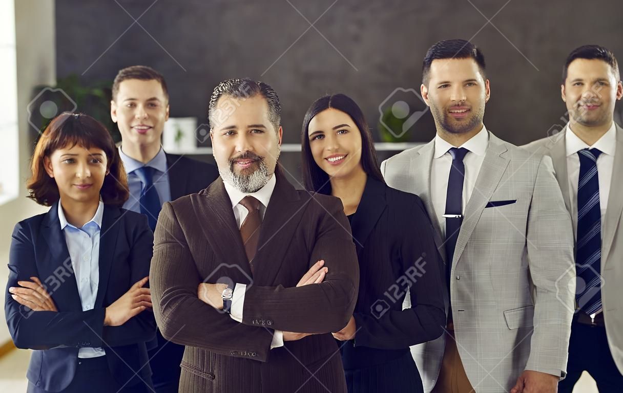Portrait of a confident adult business leader with a team of employees standing behind him. Man and his business team looking at the camera and smiling. Concept success and team spirit.