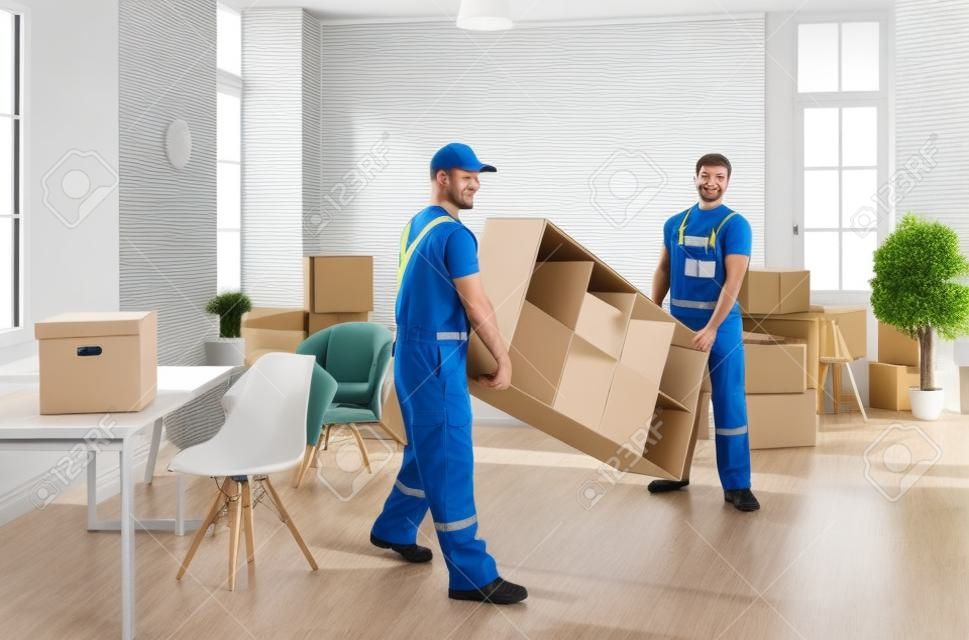 Male movers in uniform carry furniture help client with office or home settle. Deliverymen or carriers work for customer during moving or relocation. Delivery or transportation company service.