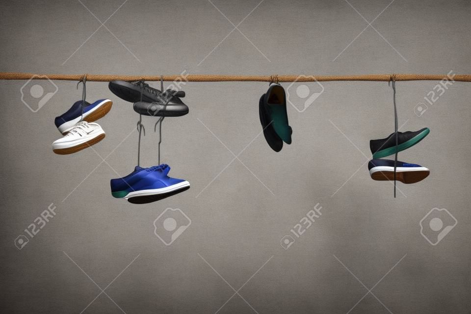 Scarpe da ginnastica vecchio e scarpe tacco alto appese al filo elettrico su sfondo contrastante