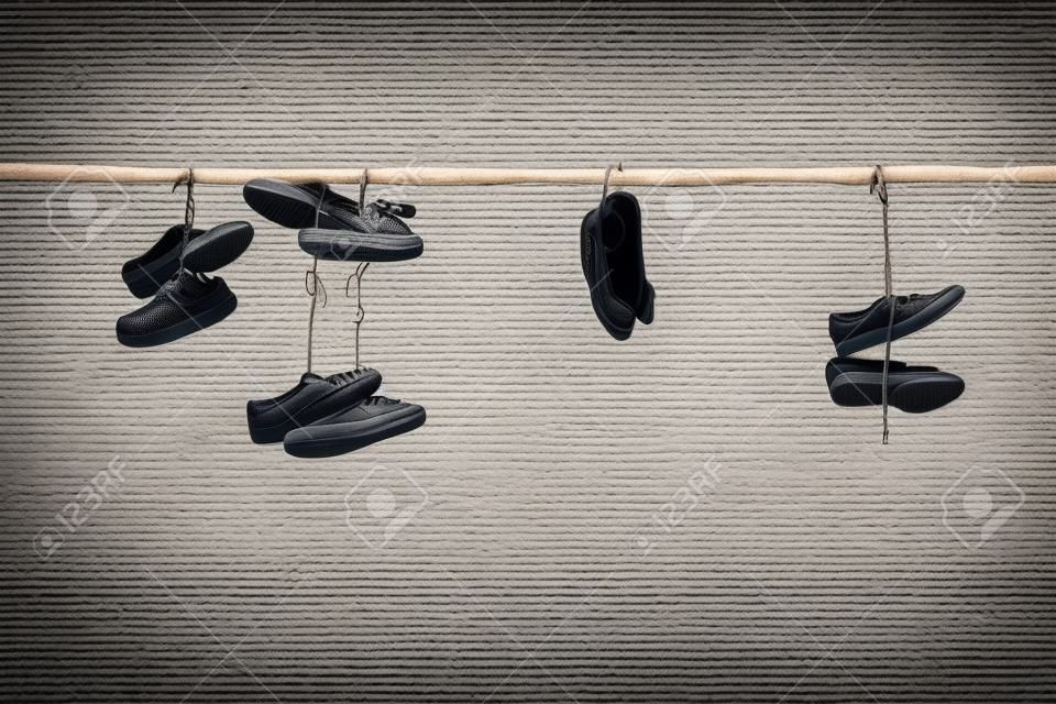 Scarpe da ginnastica vecchio e scarpe tacco alto appese al filo elettrico su sfondo contrastante