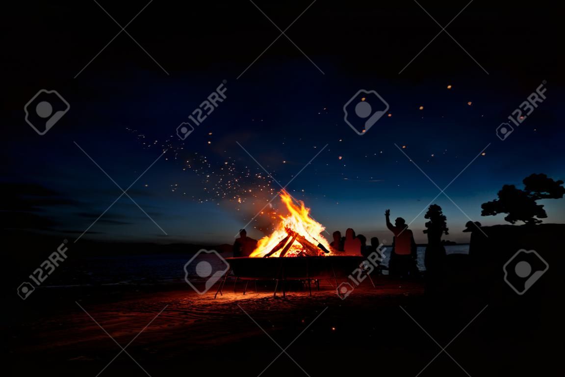 Large burning bonfire with soft glowing flame and sparkles flying all around. Romantic summer evening, people relaxing and enjoying calmness at the seaside during the Night of ancient lights.