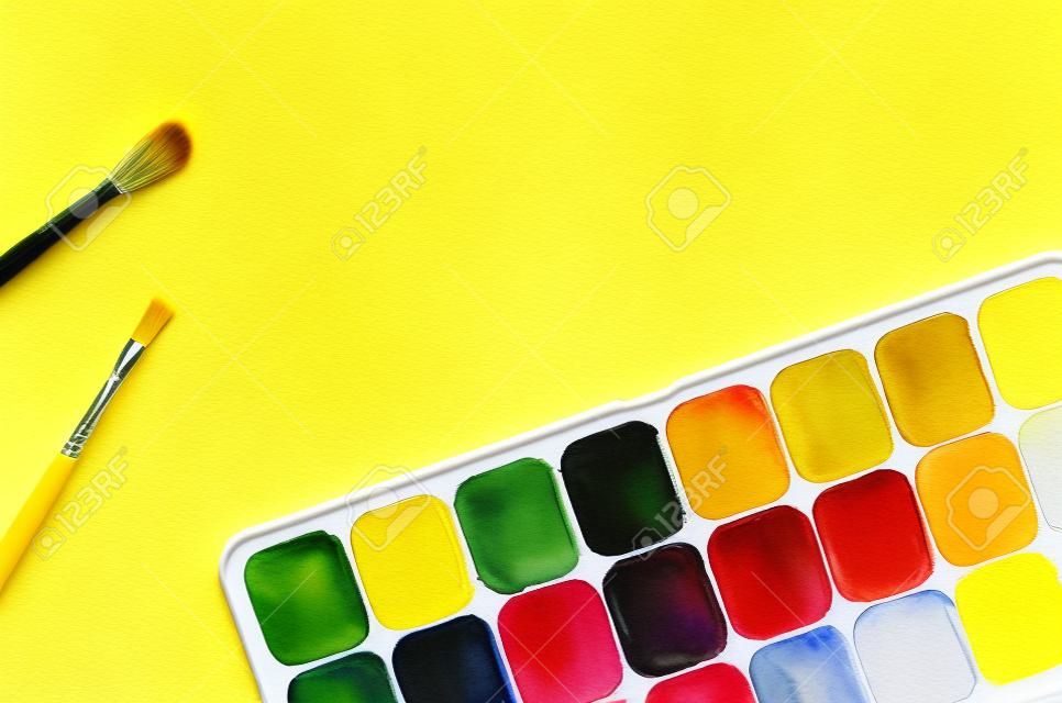 Farby akwarelowe i pędzle na żółtym tle z miejsca na kopię