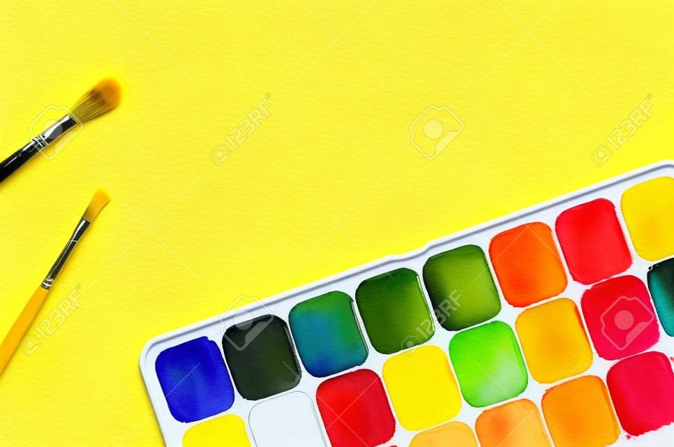 Farby akwarelowe i pędzle na żółtym tle z miejsca na kopię