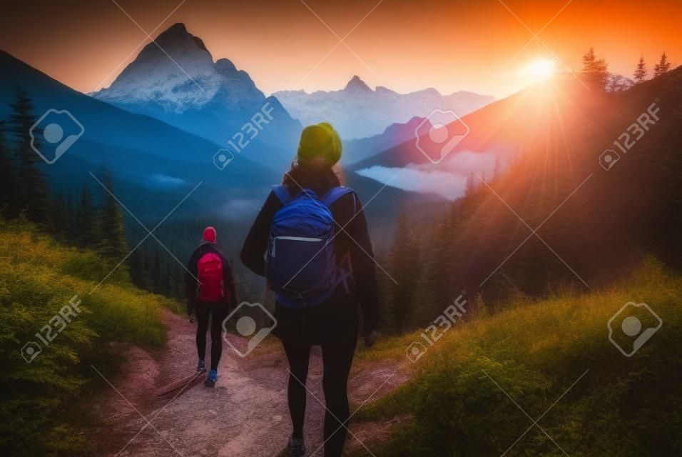 woman hiker with backpack hiking on trail in mountains at sunset.