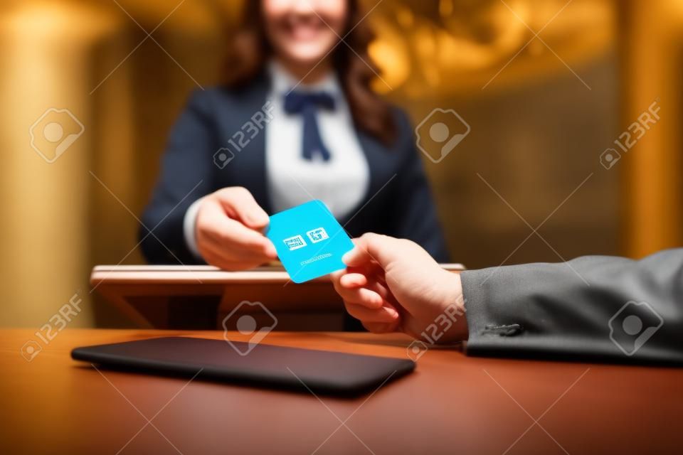 Nous vous invitons à l'essayer. Gros plan des mains masculines et féminines. Réceptionniste souriante derrière le comptoir de l'hôtel donnant la carte-clé à l'invité.