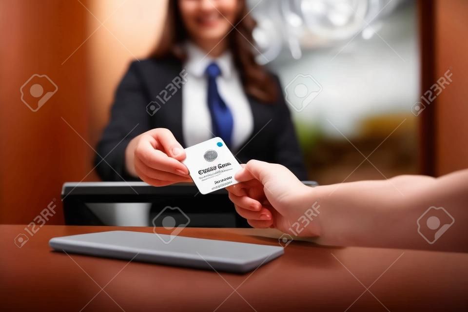 Nous vous invitons à l'essayer. Gros plan des mains masculines et féminines. Réceptionniste souriante derrière le comptoir de l'hôtel donnant la carte-clé à l'invité.