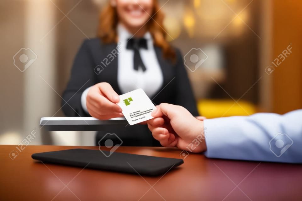Nós convidamos você a experimentá-lo. Feche acima das mãos masculinas e femininas. Recepcionista fêmea sorridente atrás do balcão no hotel que dá o cartão chave ao hóspede.