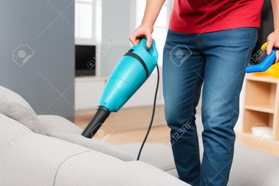 Photo recadrée d'un homme nettoyant un canapé avec un aspirateur à main tout en travaillant dans le salon. Service de nettoyage. Travaux ménagers