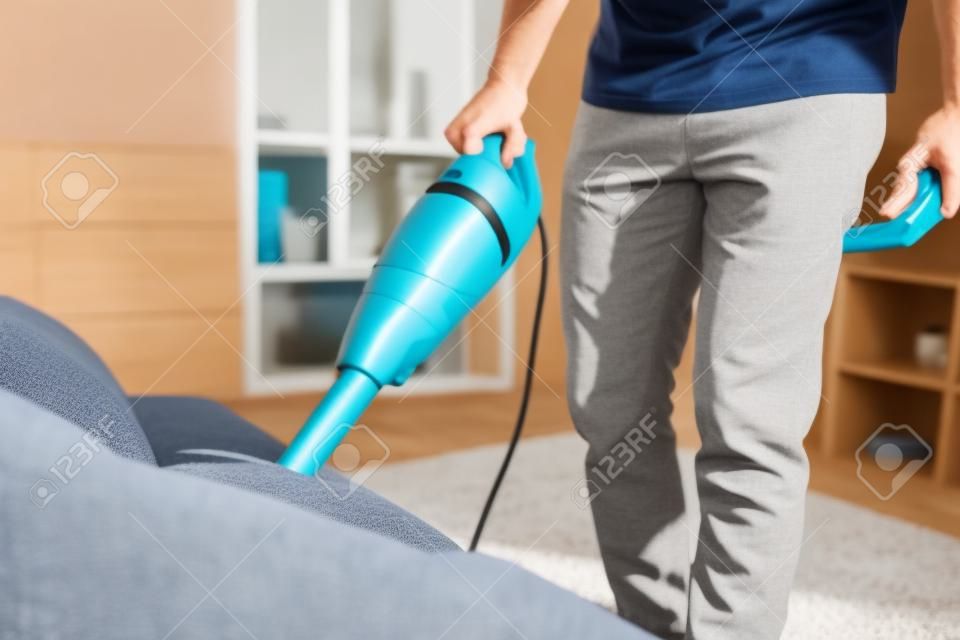 Photo recadrée d'un homme nettoyant un canapé avec un aspirateur à main tout en travaillant dans le salon. Service de nettoyage. Travaux ménagers