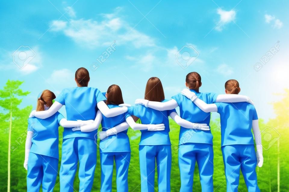 We can save the planet together. Group of young volunteers wearing uniform and rubber gloves hugging and looking at green forest in front of them, rear view